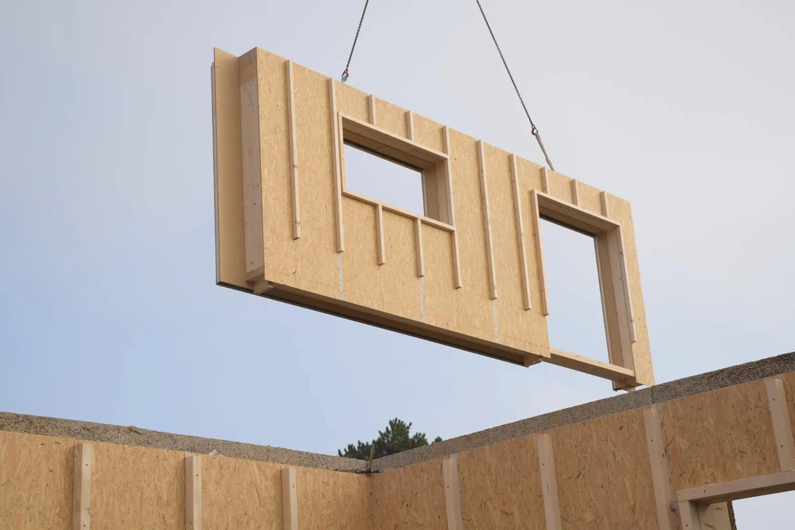 Una grúa baja un panel de pared prefabricado con aberturas para ventanas sobre la casa en construcción